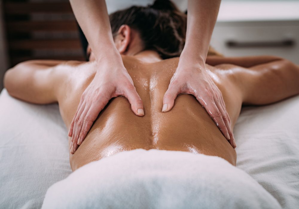 Physiotherapist massaging female patient with injured lower back muscle. Sports injury treatment.